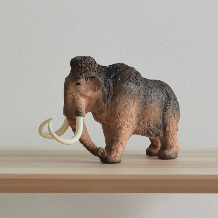 Model of a woolly mammoth on a wooden surface with a plain background