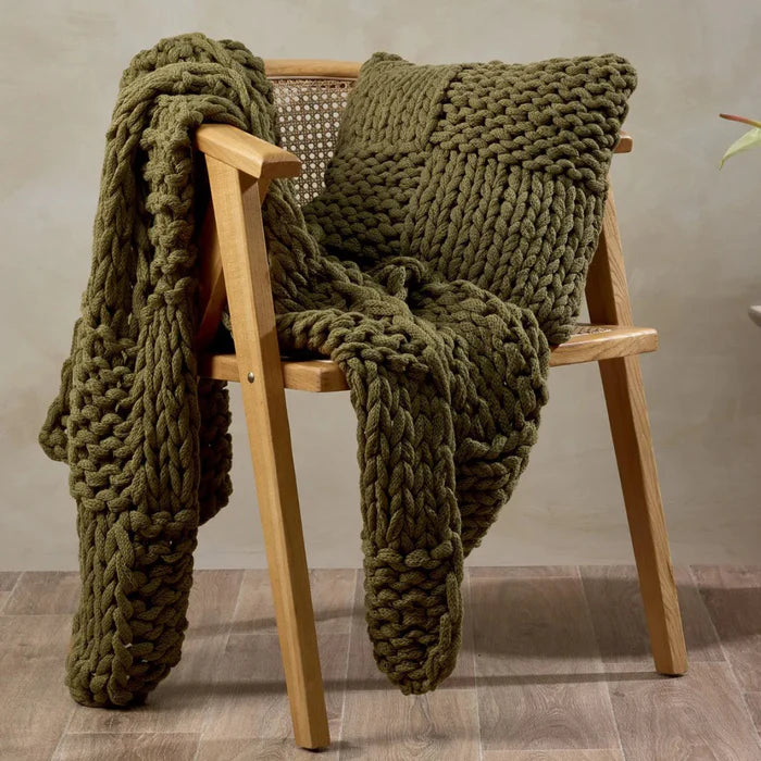 Green knitted blanket draped over a wooden chair against a neutral background