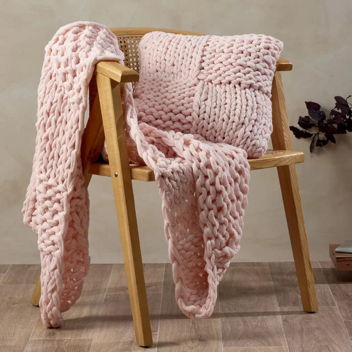 Pink knitted blanket draped over a wooden chair against a neutral wall.