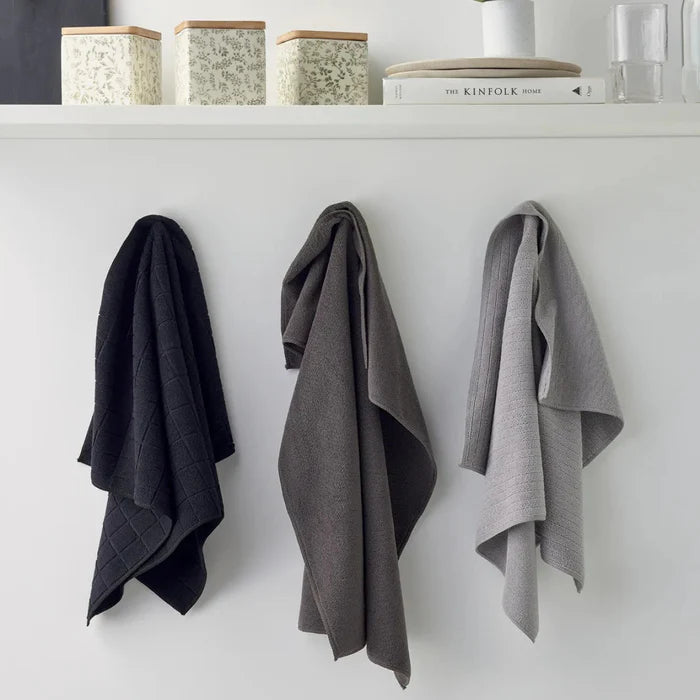 Three towels hanging on a white wall with decorative items above.