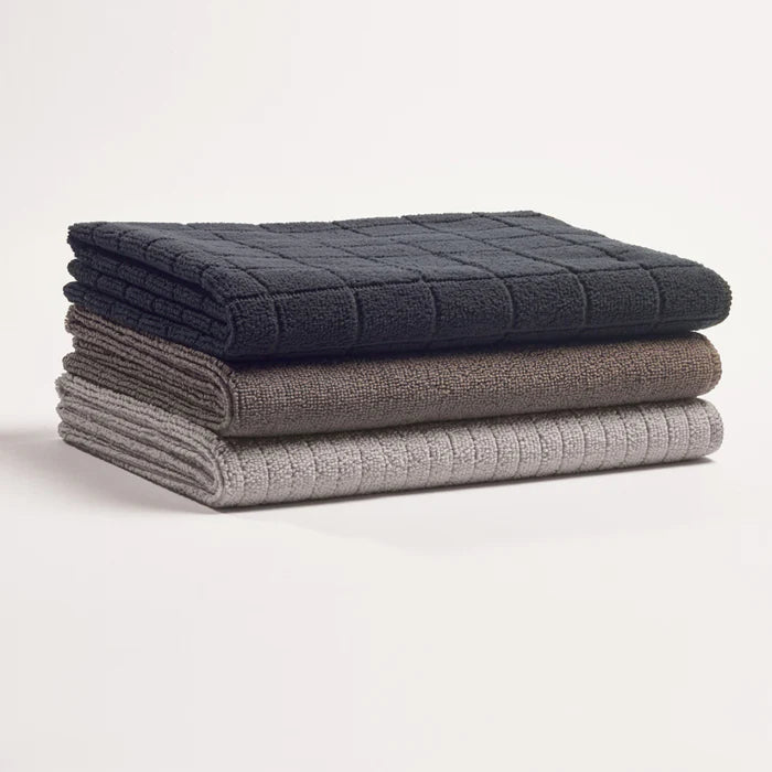 Stack of three folded towels in dark blue, gray, and light gray on a white background