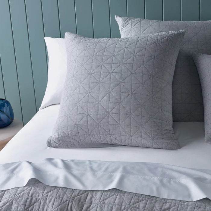 Gray quilted pillow on a bed with a blue headboard