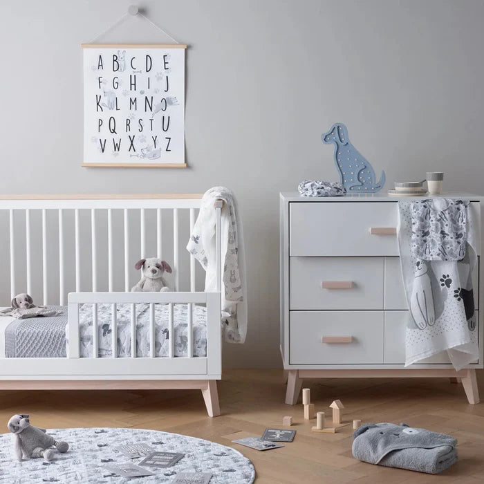 Nursery room with white crib, dresser, and toys on a wooden floor.
