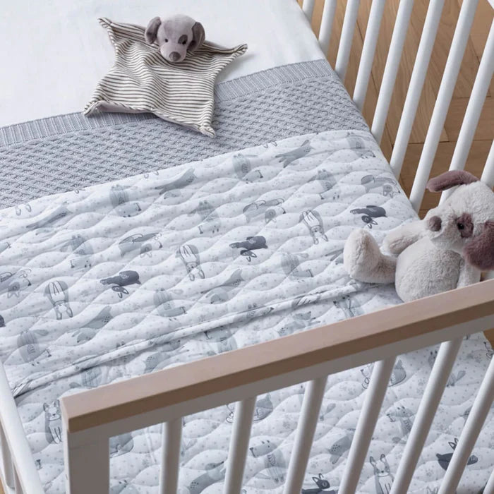 Crib with a gray quilt featuring animal prints and plush toys.