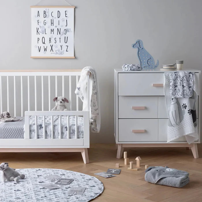 Nursery room with white crib, dresser, and toys on a wooden floor.