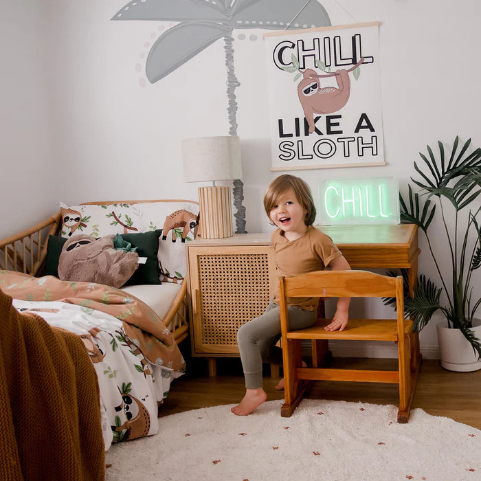 Child in a bedroom with a 'Chill Like a Sloth' sign and sloth-themed decor.