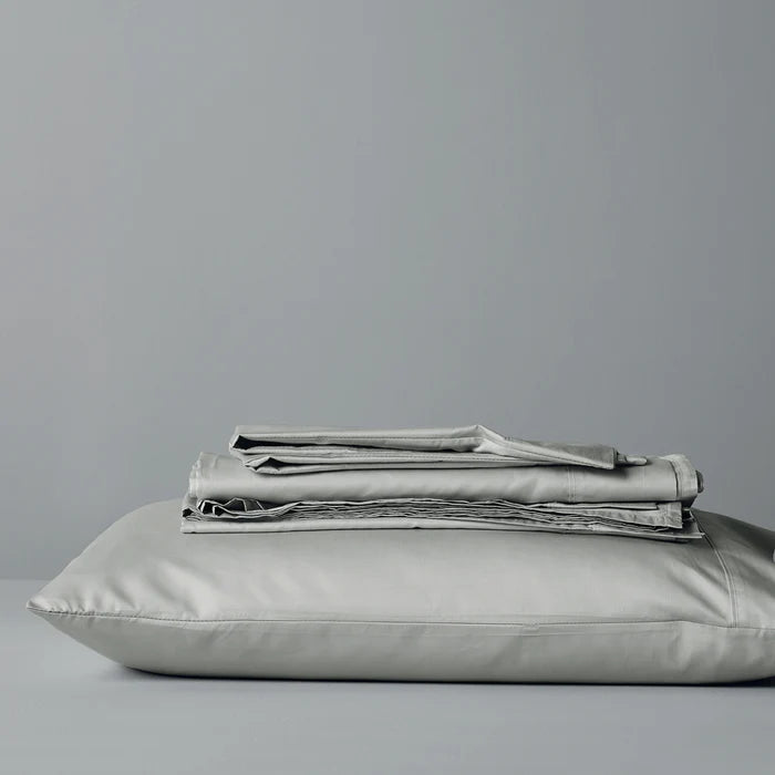 Folded light gray bedding set on a pillow against a plain background