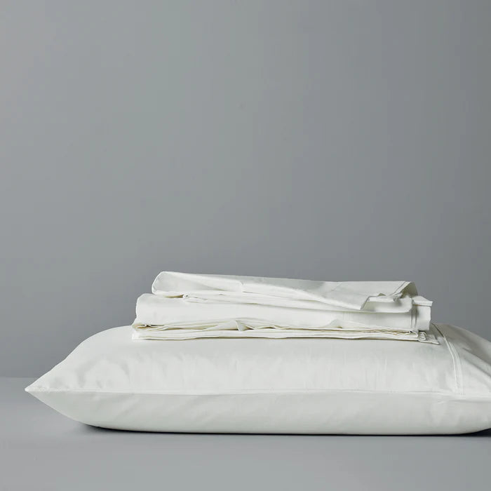 White pillow and folded white bedding on a gray background