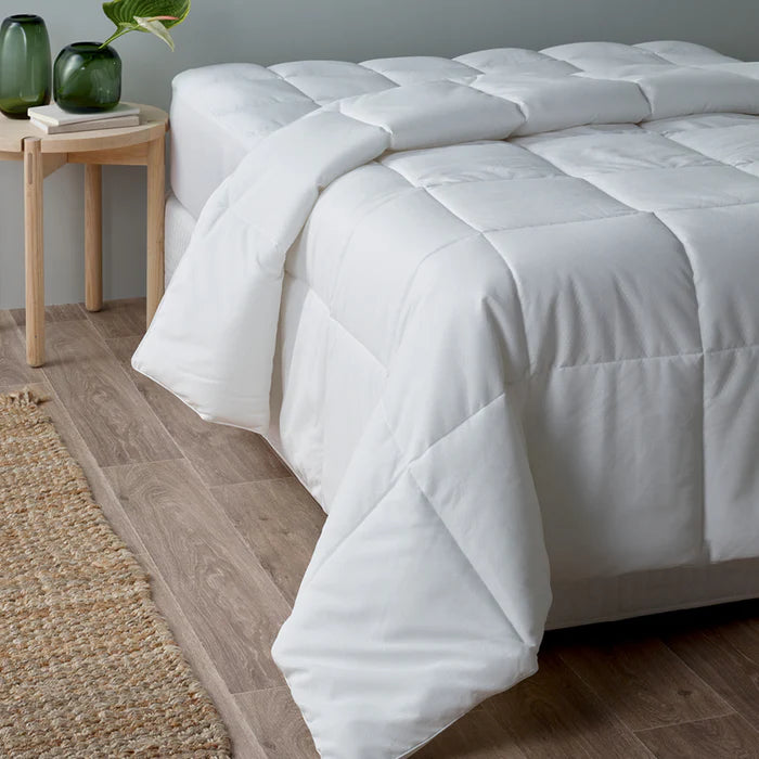 White comforter on a bed in a bedroom setting with a side table and decor items.