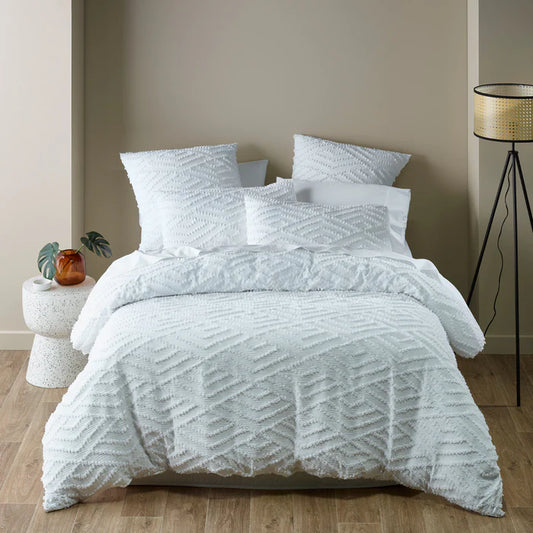 Textured white bedding set on a bed in a bedroom with a lamp and plant.