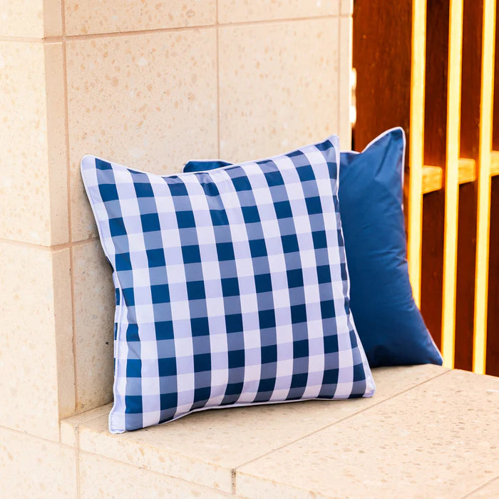 Two blue checkered pillows on a stone ledge with a tiled wall and wooden structure in the background.