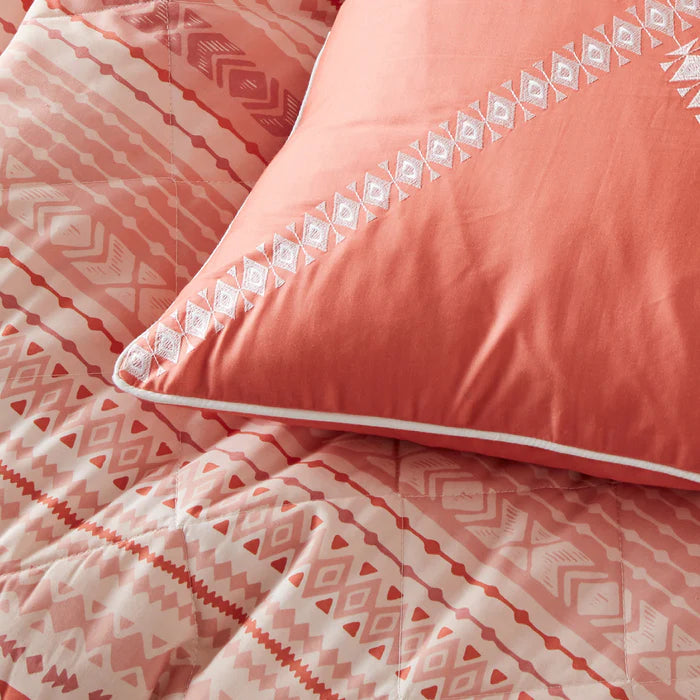 Coral bedding set with geometric patterns on a bed.