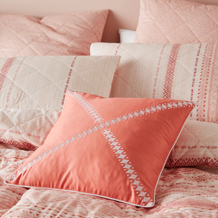 Pink and coral textured bedding with decorative pillows on a bed.