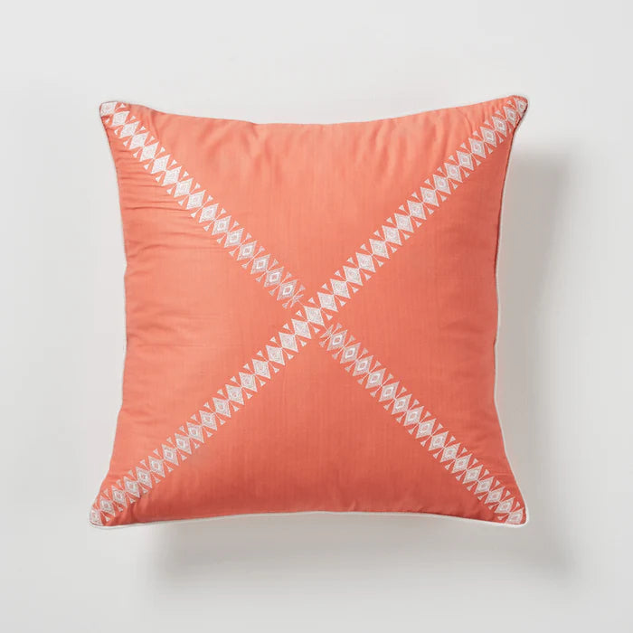Coral pillow with white geometric pattern on a light gray background